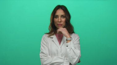 İzole edilmiş yeşil arka planda güvenle poz veren beyaz önlüklü kadın kararlılık, gençlik ve profesyonellik gösteriyor..