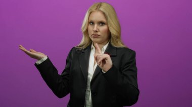 Bir kadın tek eliyle hareketler yapıyor. Durma sinyaliyle canlı mor bir arka plana karşı, dışavurumsal iletişim sergiliyor..