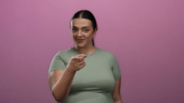 Kıvrımlı genç bir kadın, izole edilmiş pembe arka plan duvarında şakacı bir şekilde gülüyor, arkadaşlığı ve iletişimi iletiyor..