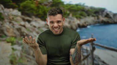 Dövmeleri olan genç bir adam plajda açık bir gökyüzünün altında kayalık bir kıyı şeridi ile anlamlı jestler yapıyor..