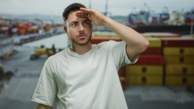 Denize bakan limanda duran sakallı genç adam, beyaz gömlekli, arka planda gemi ve konteynırlar olan, macera ve keşif hissi yakalayan.