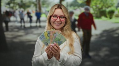 Açık havada gülümseyen bir kadın, elinde Romen leu banknotlarıyla güneşli bir caddede bulanık şehir sakinlerinin arasında bir neşe ve zenginlik anı yakalıyor..