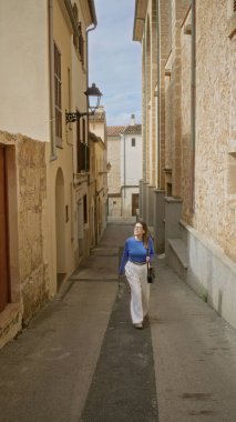 Mallorca 'nın eski kasabasında, temiz gökyüzünün altında büyüleyici dar bir sokakta yürüyen bir kadın, Akdeniz mimarisinin ve canlı kültürel atmosferinin özünü yakalıyor..