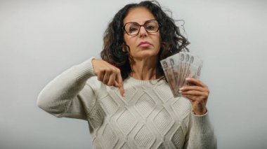 Beyaz bir arka plan duvarına Rus rublesi dayamış orta yaşlı bir kadın, olumsuz duygularını ifade ediyor ve finans, para ve para kavramlarını vurguluyor..