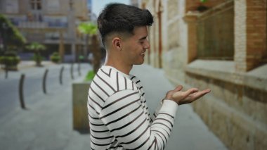 Canlı bir şehir caddesinde uzanmış ellerini uzatarak gülümseyen İspanyol adam, şehir yaşamını ve açık hava cazibesini çekici ve çekici bir şekilde sergiliyor..