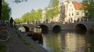 Amsterdam Kanalı yakınlarındaki bulanık bir kadın uzak köprüsü ve bisikletleriyle Hollanda şehir manzarasının dağılmış atmosferini vurguluyor..