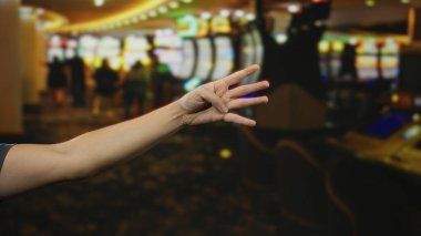 Dört parmağı olan bir adam canlı kumarhane ortamında etrafı renkli kumar makineleriyle çevrili ve canlı bir kumarhane ortamı yaratıyor..