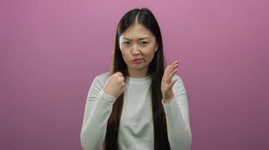 Kapalı yumruklarla canlı pembe bir arka plana karşı kararlılığını ifade eden bir kadın izole edilmiş bir stüdyo ortamında güç ve direnç gösteriyor..