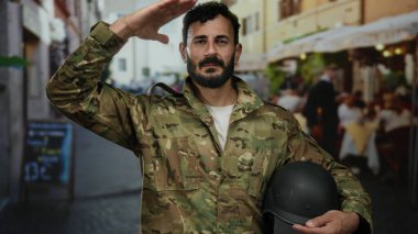 İspanyol üniformalı bir adam canlı bir sokak ortamında selamlıyor, miğfer tutuyor, cesaretini ve kamu hizmetini vurguluyor..