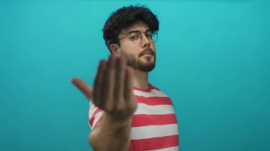 Sakallı ve gözlüklü genç İspanyol adam mavi arka plana karşı parmak işareti yaparak buraya gelir..