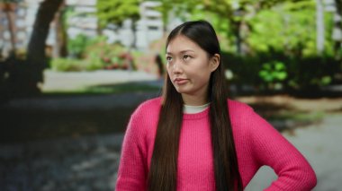 Açık havada pembe giyinmiş bir kadın yemyeşil bir parkta gülümsüyor doğal güzelliğini ve kendine güvenini sergiliyor..