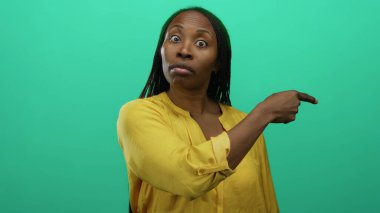 Sarı bluzlu, uzun saçlı, yeşil bir arkaplanı işaret eden, kendine güvenen ve dışlanmış bir arkaplanın önünde duran bir kadın..