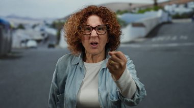 Hispanik kadın, bulutlu bir günde günlük kot pantolon ve gözlük giyip, duygularına ve kentsel çevresine vurgu yaparak şehir caddesinde öfkesini ifade ediyor..