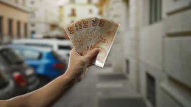 Bir şehir caddesinde elinde Türk lirası banknotları tutan adam şehir ortamında ticaret ve finans ruhunu yakalıyor..