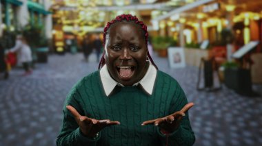 Kalabalık şehir sokak ortamında tutkuyla bağıran bir kadın, bulanık kentsel geçmişe sahip yeşil bir kazak giyiyor, hayal kırıklığını ya da öfkeyi ifade ediyor, heyecan verici duyguları canlı bir şekilde ifade ediyor..