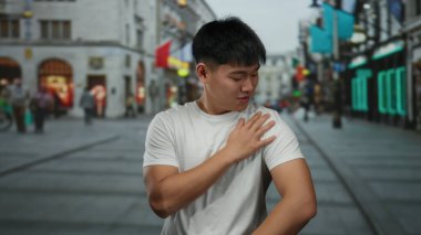 Genç Çinli bir adam gülümsüyor ve hareketli bir şehir caddesinde sokak ortasında el kol hareketi yapıyor..
