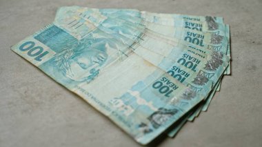 Somut bir zemine yığılmış 100 reais 'lik Brezilya banknotları para birimini vurguluyor ve ülkenin mali temsilini gözler önüne seriyor..