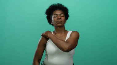 İzole edilmiş yeşil bir arka plana karşı omuz ağrısı hisseden kadın, sağlık ve sağlık bilincini vurgulayan yakın plan bir portrede rahatsızlık ve gerginlik gösteriyor..