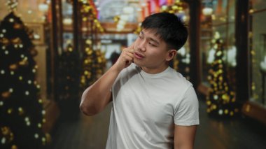 Şehir caddesinde genç bir adam akıllı bir telefonla konuşuyor. Tatil süslemeleri ve parlak ışıklar arasında, günlük beyaz bir gömlek giyiyor, kentsel şenlik ve teknoloji taşıyor..