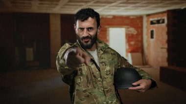 İspanyol üniformalı bir adam bir inşaat sahasında elinde miğfer tutarak kısmen inşa edilmiş iç kısımda odaklanmış bir ifade sergiliyor..