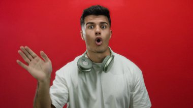 Kulaklıklı genç bir adam kırmızı arka planda şakacı hareketler yapıyor, enerjik ve hayat dolu bir havayı modern ve şık bir şekilde yakalıyor..