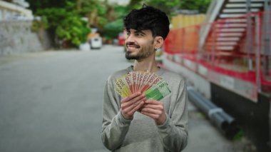 Norveçli kronu elinde tutan adam şehir sokaklarında çeşitli duygular ifade ederek para ve modern yaşam tarzını gözler önüne seriyor..