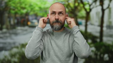 Parktaki sakallı adam kulaklarını kapatıyor. Dışarıdaki hayal kırıklığını şakasına anlatıyor..