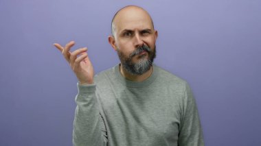 Sakallı yakışıklı kel adam, izole edilmiş mor arka plana karşı gizli bir jest yapar. Gizlilik ya da gizemi ifade eden yüzü ve ince el hareketiyle aktarır..