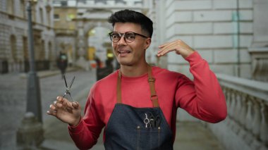 Şehrin caddesinde elinde makas tutan genç İspanyol adam gözlüklü önlüklü gülümsüyor. Dışarıdan kendine güvenen dış plan resmine benziyor..