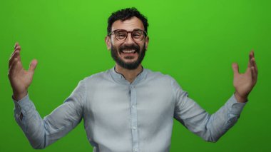 Gözlüklü, sakallı, yeşil arkaplan önünde heyecanını ifade eden, açık renk tişörtlü İspanyol bir adam..