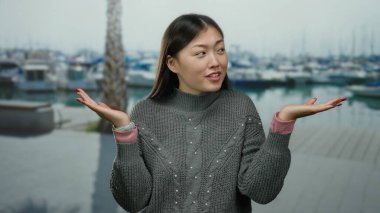 Arka planda tekneleri olan, sakin bir liman manzarasında sakin bir süveter ve izle gülümseyen, sakin bir kadın..