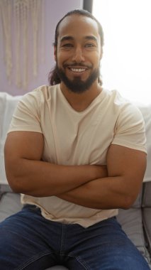 Sıcak bir oturma odasında oturan bir adam, kollarını kavuşturmuş, kendine güveni ve sıcaklığı yayıyor, rahat bir iç mekan atmosferi yakalıyor..