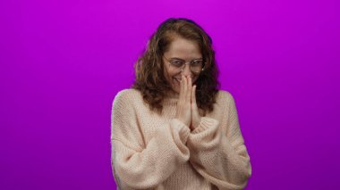 Pembe kazaklı, elleri parlak mor arka planda gülümseyen bir kadın izole edilmiş bir stüdyo ortamında sıcaklığı ve mutluluğu taşıyor..