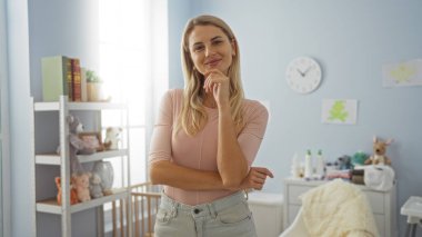 Işıklı duvarları ve bebek dekoru olan rahat yatak odasında kendine güvenen bir kadın zarif mobilyalar ve dekoratif unsurlarla huzurlu bir iç dekorasyon sergiliyor..