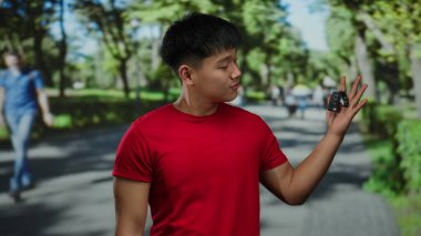 Kırmızı gömlekli genç adam yeşil bir parkta gülümseyen araba anahtarı taşıyor. Mutluluk ve özgürlük taşıyor..