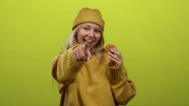 Elinde kurabiyeyle gülümseyen ve parlak yeşil arka planda kameraya bakan bir kadın..