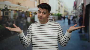 Şehrin hareketli bir caddesindeki terasta duran adam rahat bir restoranın önünde açık şehir ortamında rahat ve kendinden emin bir hava yayıyor..