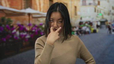 Kalabalık bir şehir caddesinde, açık bir restoran terasında el kol hareketi yapan Çinli genç bir kadın..