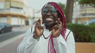 Pembe örgülü bir kadın, şehir sokaklarında neşeyle gülümsüyor, iyimserliğini ve iyimserliğini dile getiriyor..