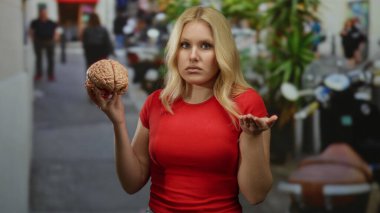 Şehrin işlek caddesinde elinde model beyin tutan genç bir kadın. Kırmızı gömleğinin gelişigüzel görünüşüne zıt olarak karışık şehir geçmişiyle kargaşa ve merakı yansıtıyor.