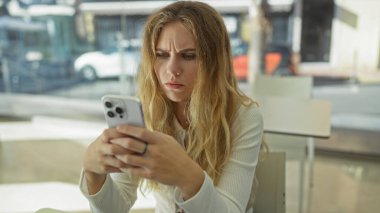 Gündüzleri masa başında otururken modern dekorasyonla akıllı telefona odaklanmış bir kadın..