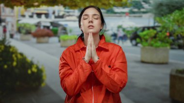 Hapishane tulumu giymiş esmer kadın ve kelepçeli kadın sokakta, dışarıda dua ediyor, halka açık bir ortamda hassasiyet ve gücü harmanlıyor..