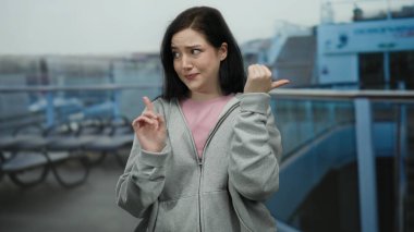 Esmer saçlı ve şaşırmış yüz ifadesi olan bir kadın gemi güvertesinde geriye dönük işaret ediyor. Görülmemiş bir şey hakkında merak veya kafa karışıklığı olduğunu söylüyor..