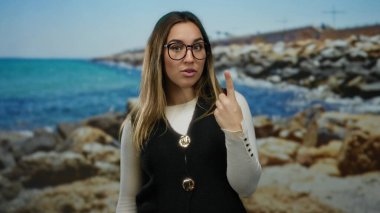 Güneşli bir plajda neşeli bir ifadeyle kutluyor, sarışın, gözlüklü, sakin deniz manzarasının ortasında heyecanlı görünen bir kadın..