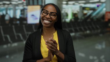Havaalanı terminalinde gözlüklü, sarı tişörtlü ve siyah ceketli bir kadın hareketli bir ruh hali ve hareketli bir evin içinde seyahat beklentisi yakalıyor..
