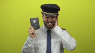 Mutlu pilot üniforması giyiyor, gülümsüyor ve elinde parlak sarı arka planda Avustralya pasaportu var.