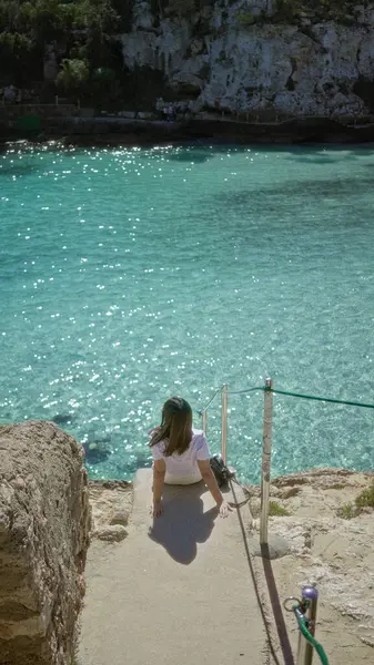 Güneşli bir günde Mallorca 'da turkuaz suları olan Cala Lombars plajının keyfini çıkaran kadın, Akdeniz sahilinin sükunetini ve doğal güzelliğini vurguluyor..