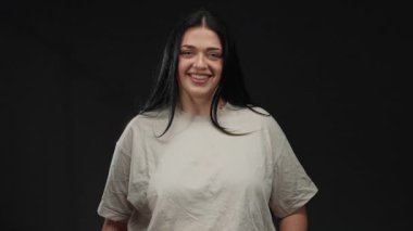 İzole edilmiş siyah bir arka plan duvarına güvenle gülümseyen bir kadın, büyük beden modasını ve neşeli aurasını vurguluyor..