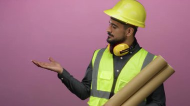 Güvenlik temalı İspanyol adam pembe arka planda mimar temalı jestler yapıyor..