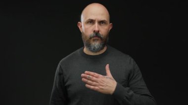 Kel, koyu renk gömlekli bir adam elini göğsüne koyuyor. Siyah bir arkaplana yaslıyor. Samimiyet ve kendine güveni izole stüdyo ortamında resmediyor..